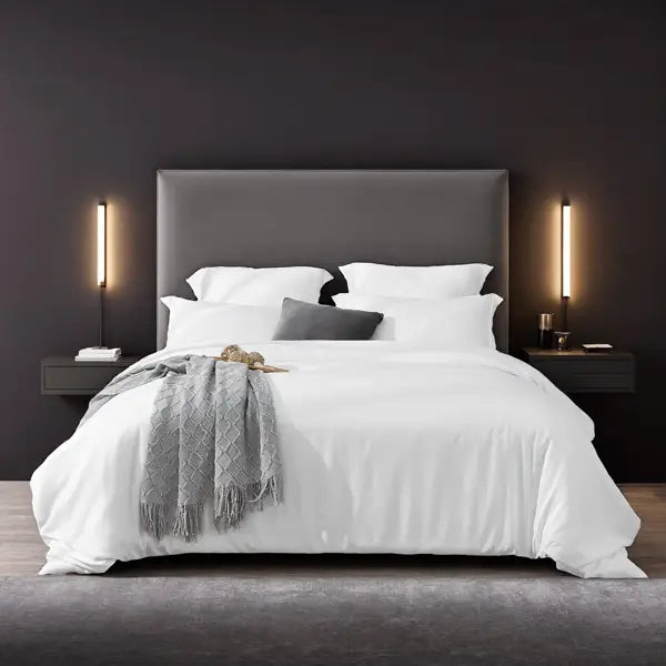 Gray upholstered bed frame featuring a white oversized duvet cover set with pillowcases and a gray textured throw blanket draped across it.