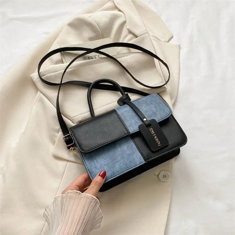 A stylish two tone denim patchwork crossbody bag featuring black and blue denim-like panels stitched together for a modern look.