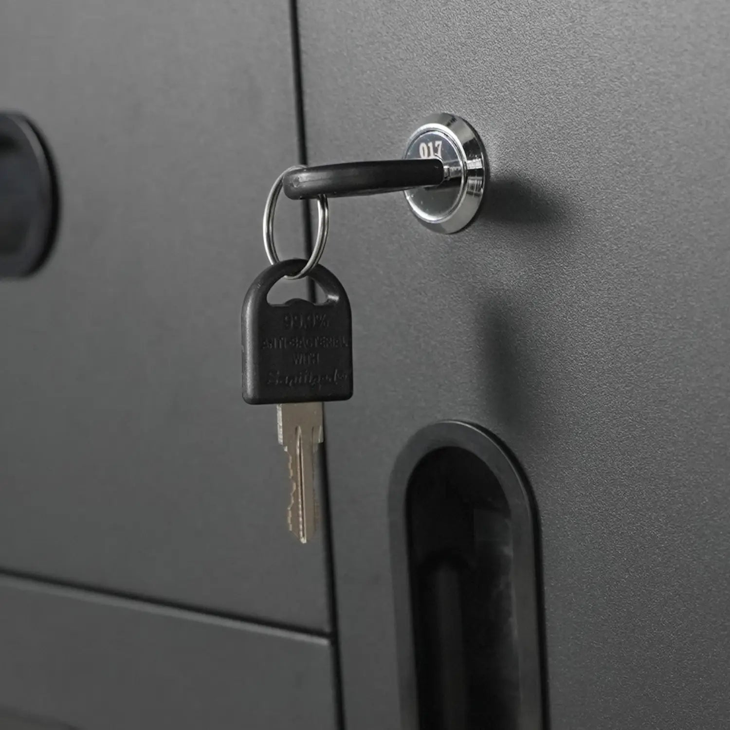 black plastic key with silver metal blade inserted into chrome lock on dark gray metal tool storage cabinet with 4 drawers and wheels