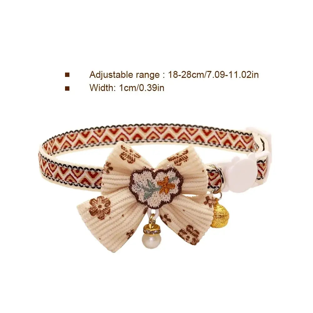 Adjustable length cream-colored floral cat collar with textured bow, embroidered heart, pearl drop, and gold-toned bell