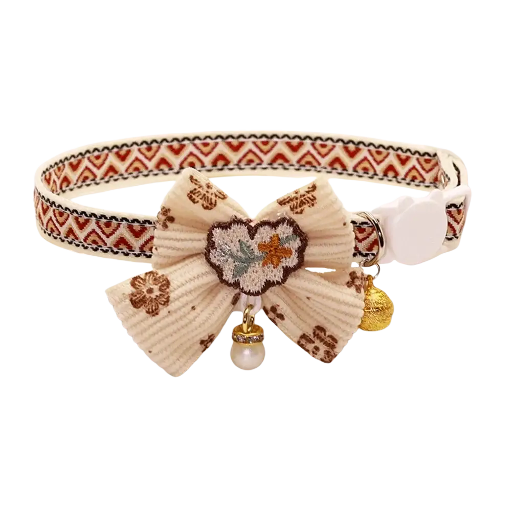 Adjustable length cream-colored floral cat collar with textured ribbon, embroidered bow, golden bell, and pearl charm