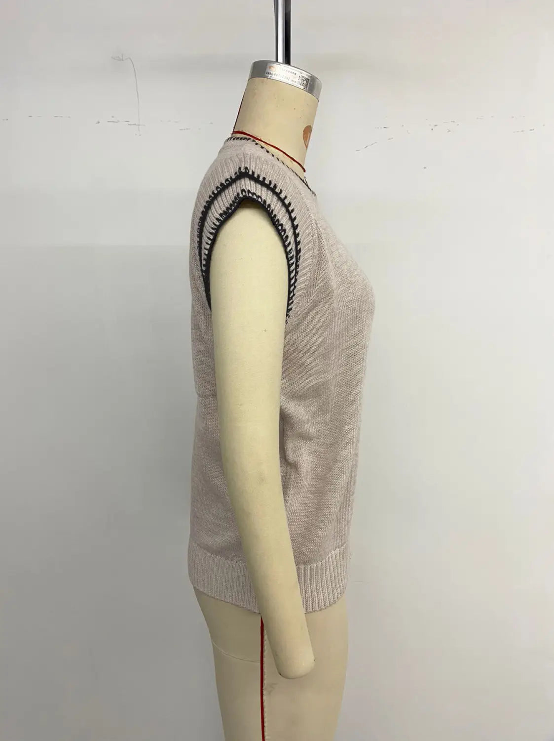 Pull sans manches en maille beige clair, présentant un passepoil contrastant noir et blanc le long des épaules et de l’ourlet.