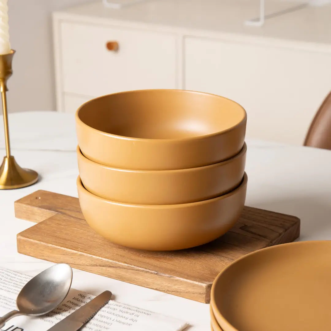 Stack of matte mustard-yellow ceramic bowls from a 12 piece stoneware dinnerware set with matte glaze designed for four.