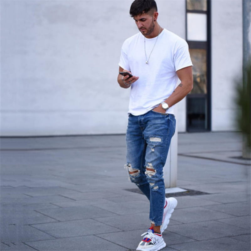 A man wearing a white t-shirt and men’s distressed blue denim ripped knee jeans.
