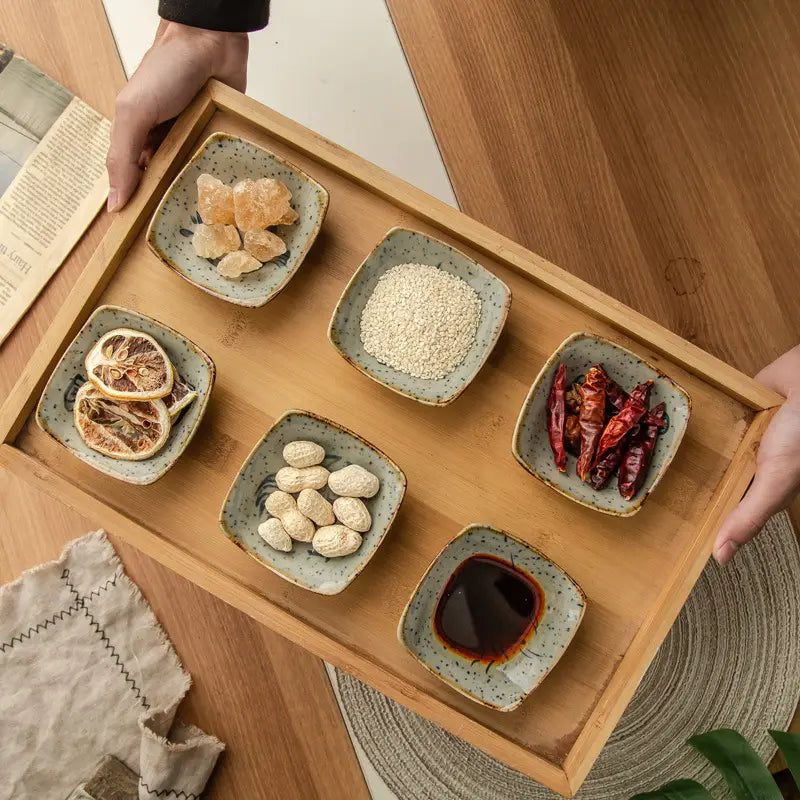 Light green ceramic square bowls with speckled glaze arranged on a wooden tray in a Japanese style ceramic sea creature sauce dish set.