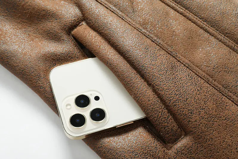 Un iPhone blanc, doté d’un système de caméra à triple objectif, dépassant de la poche d’une veste en denim doublée de polaire d’hiver pour homme, en peau de mouton, en cuir marron.