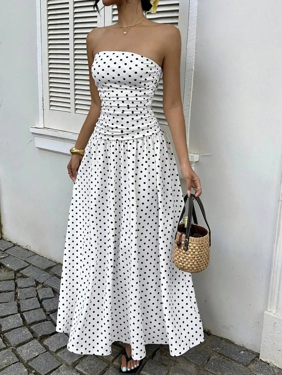 A white strapless maxi dress with black polka dots and a ruched waist designed as a polka dot off shoulder strapless maxi dress.
