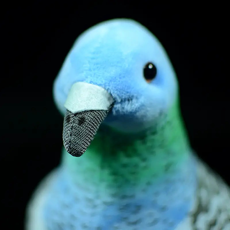 Une peluche de colombe bleue et verte mesurant 19 cm, avec un bec noir texturé conçu comme une poupée d’oiseau