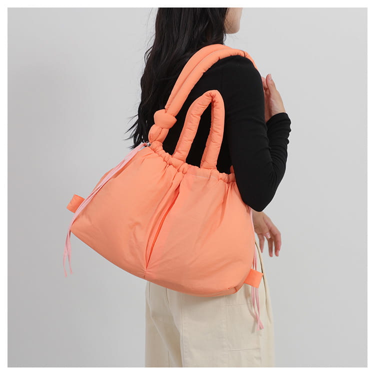 a soft puffy peach-colored quilted puffer tote bag made of lightweight nylon featuring thick knotted handles and drawstring ties for shoulder use