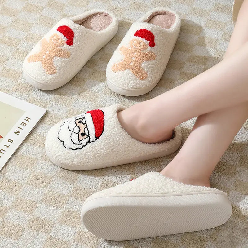 Cream-colored plush winter slippers made from soft fleece material featuring embroidered Santa and gingerbread man designs with red hats.