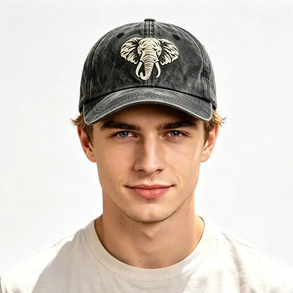 A dark gray distressed denim baseball cap made of vintage washed cotton featuring a detailed cream-colored embroidered elephant design.