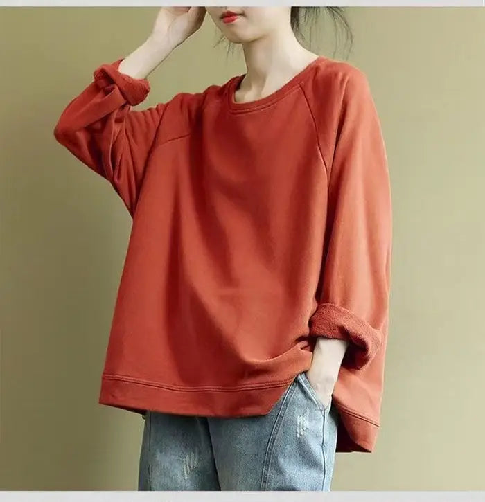 A soft rust-colored women’s relaxed oversized cotton blend pullover sweatshirt with long sleeves and rolled-up cuffs.