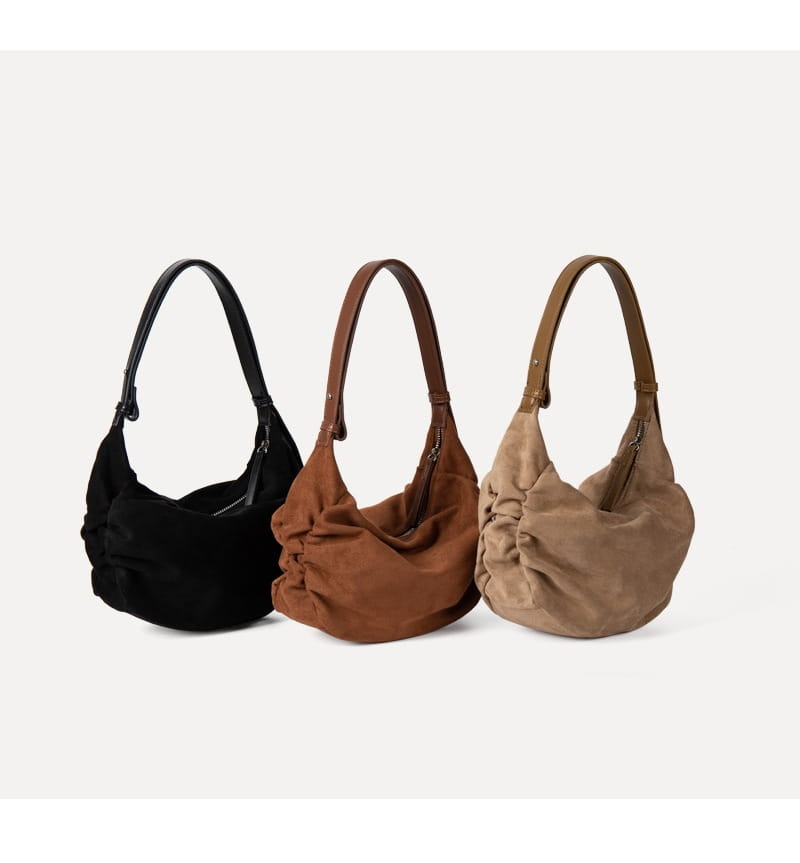 Three suede dumpling shoulder bags in black brown and tan with matching leather straps feature a slouchy crossbody hobo design.