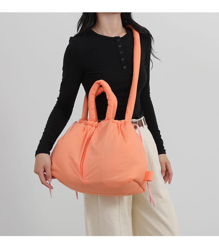 A plush peach-colored quilted puffer tote bag made of lightweight nylon with soft rounded handles and a drawstring closure.