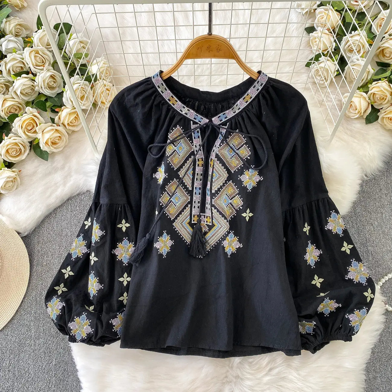 Black embroidered lantern sleeve tie neck blouse with intricate geometric patterns in gold silver and light blue thread featuring a tie-front detail and tassels.