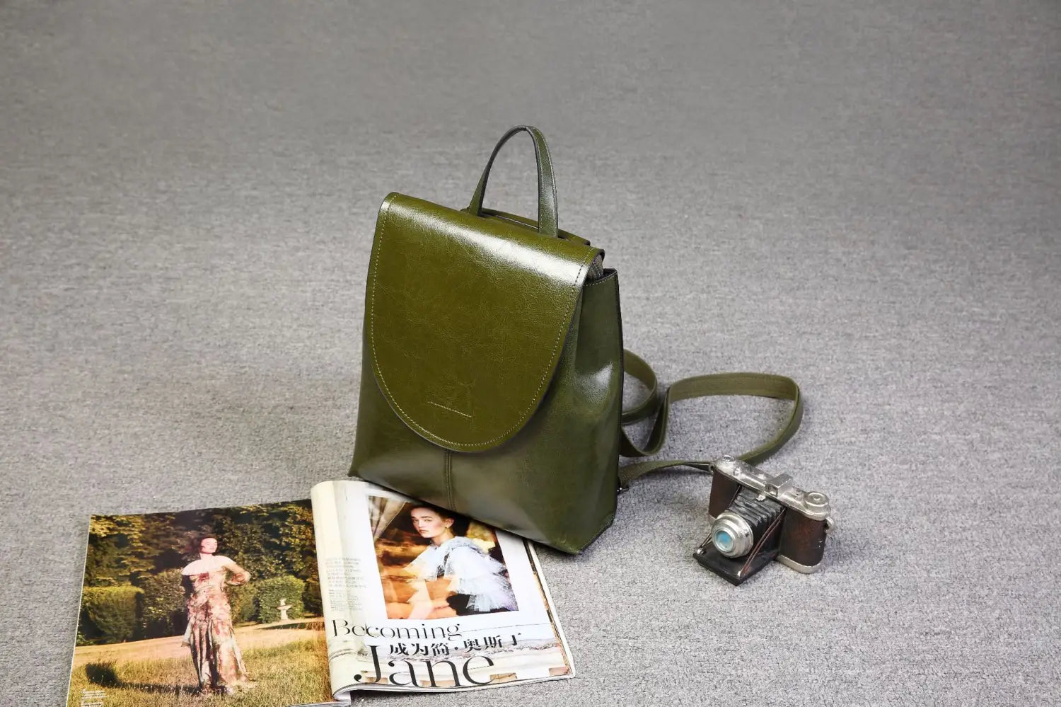 Mochila bandolera de cuero en color verde oliva, con cierre de solapa y correa de hombro ajustable, adecuada para el uso en moda retro.