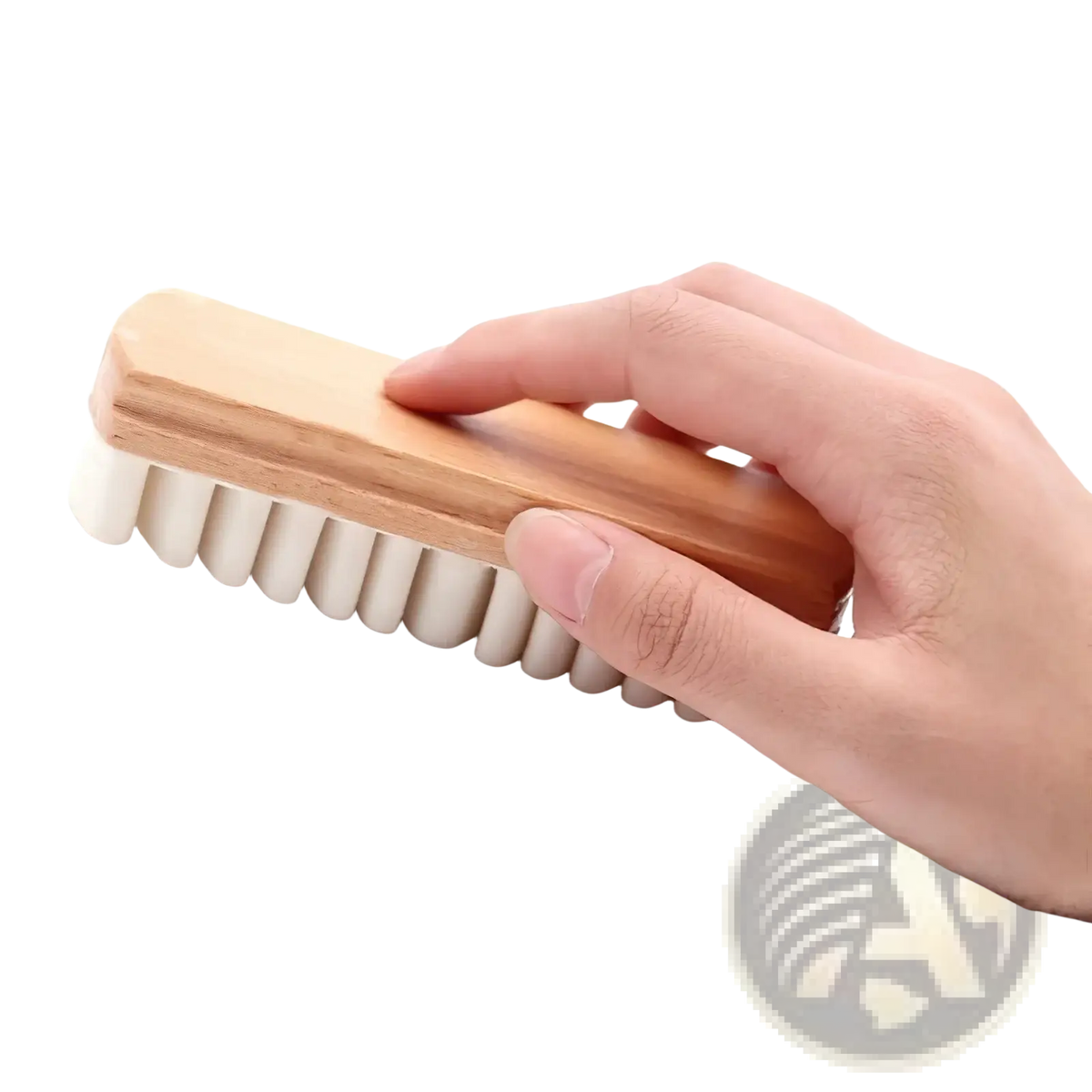 A hand holds a light brown wooden alcantara suede car interior cleaning brush with dense off-white bristles