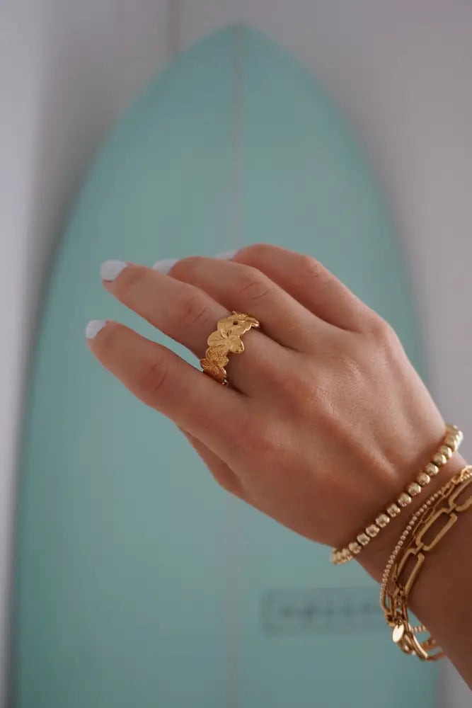 A gold-toned Aloha Gold tropical flower statement ring with intricate leaf-like design worn on a finger