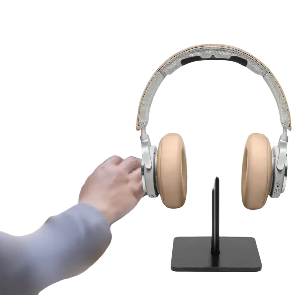 Silver and beige over-ear headphones resting on an aluminum headphone stand with soft silicone headset holder top