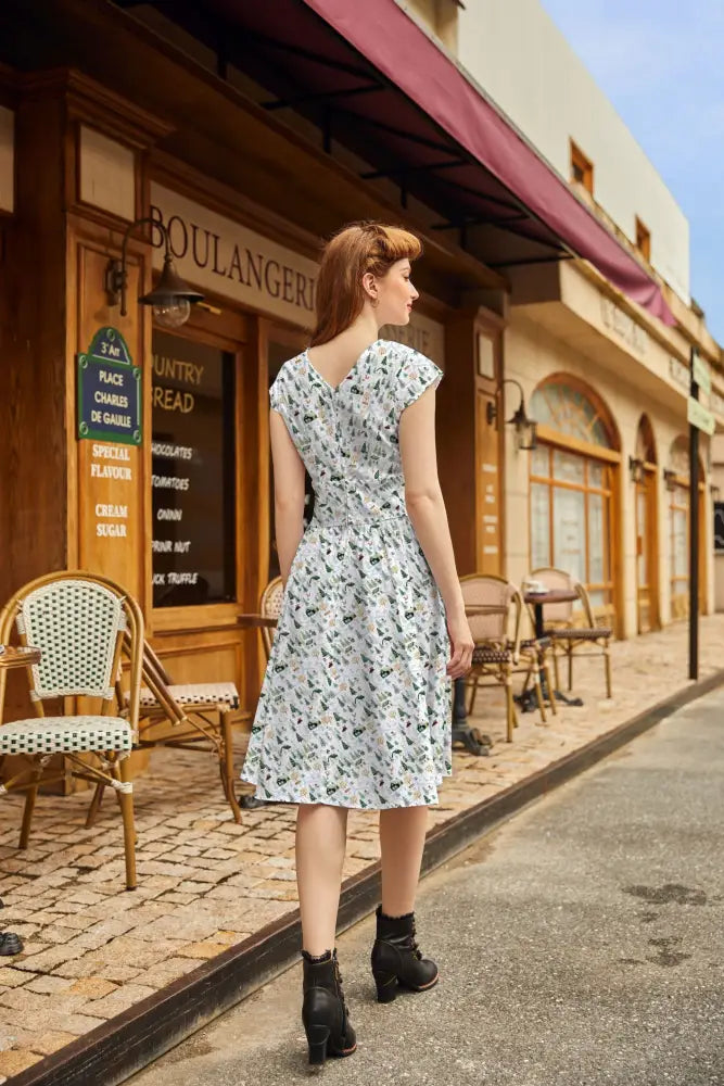 A woman wears an animal town greta v-neck cotton holiday dress in white with black floral patterns and short sleeves