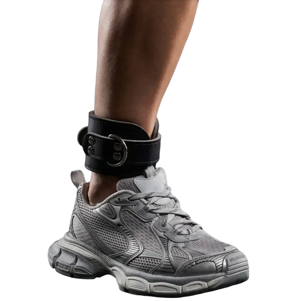 Black leather ankle strap with silver buckle and dual-plate design worn with gray mesh sneaker for strength training