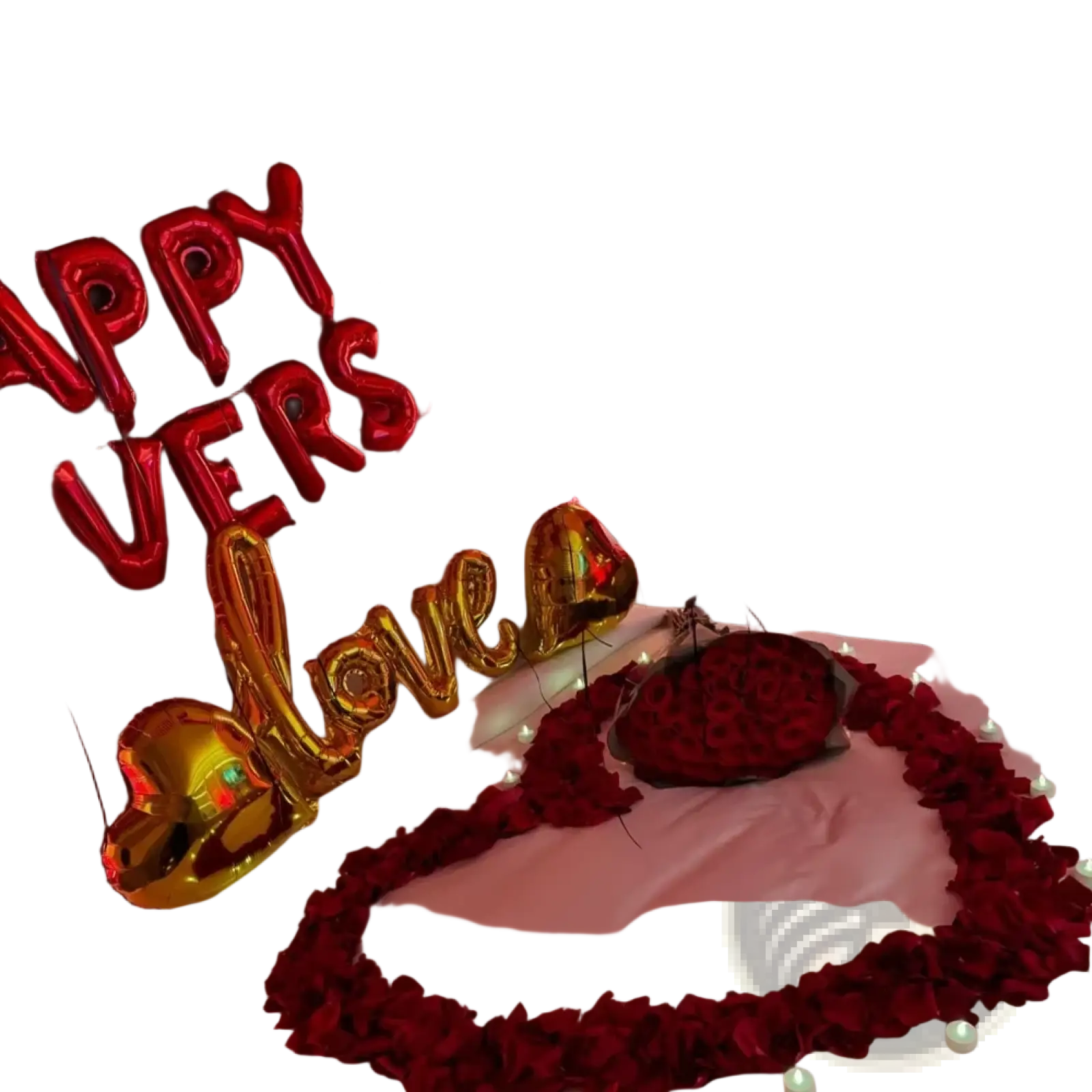 Red and gold foil balloon letters spelling happy anniversary and love above bed decorated with red heart balloons and rose petals