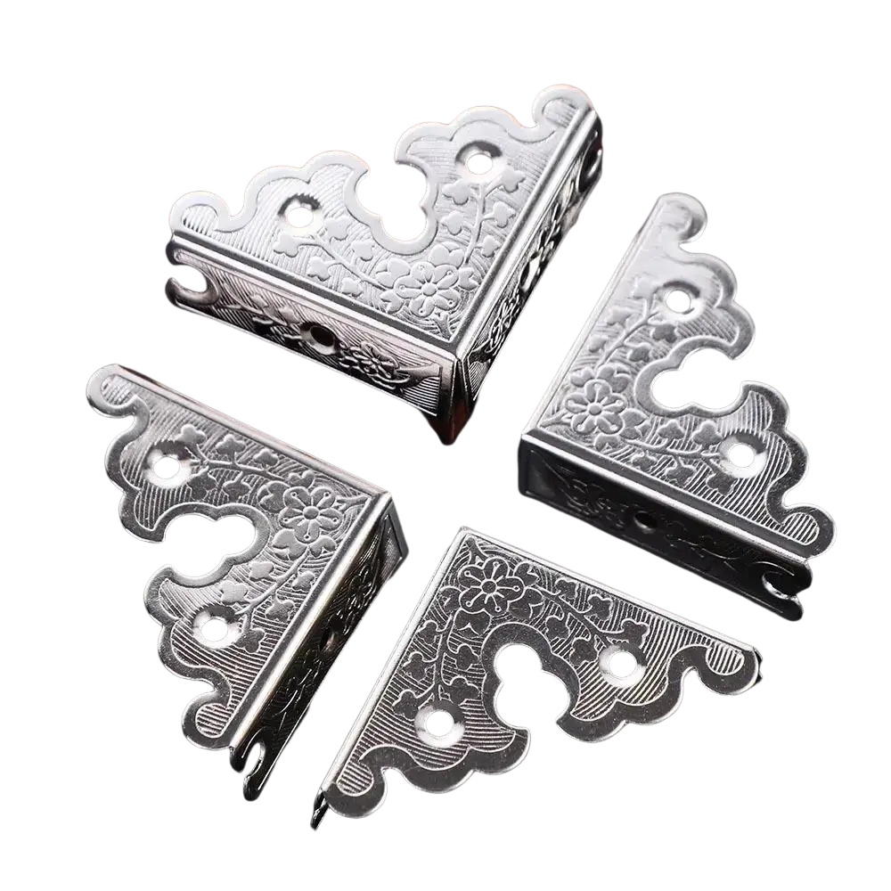 Silver decorative corner brackets with intricate floral engravings and scalloped edges as a furniture protector