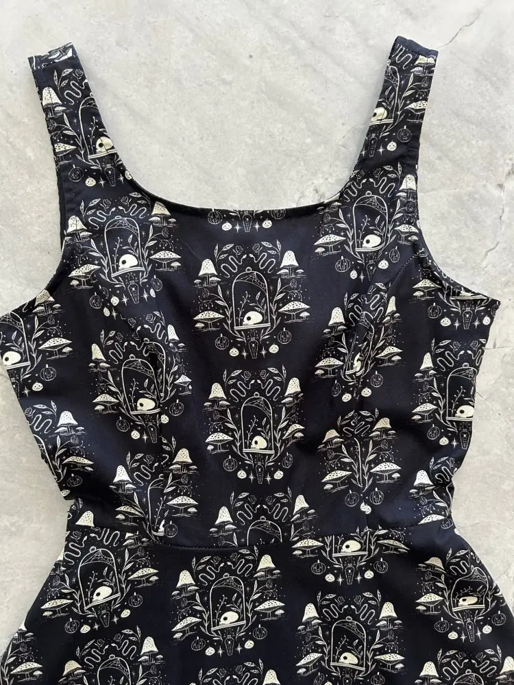 Black sleeveless apothecary skater dress with white whimsical mushroom and skull illustrations