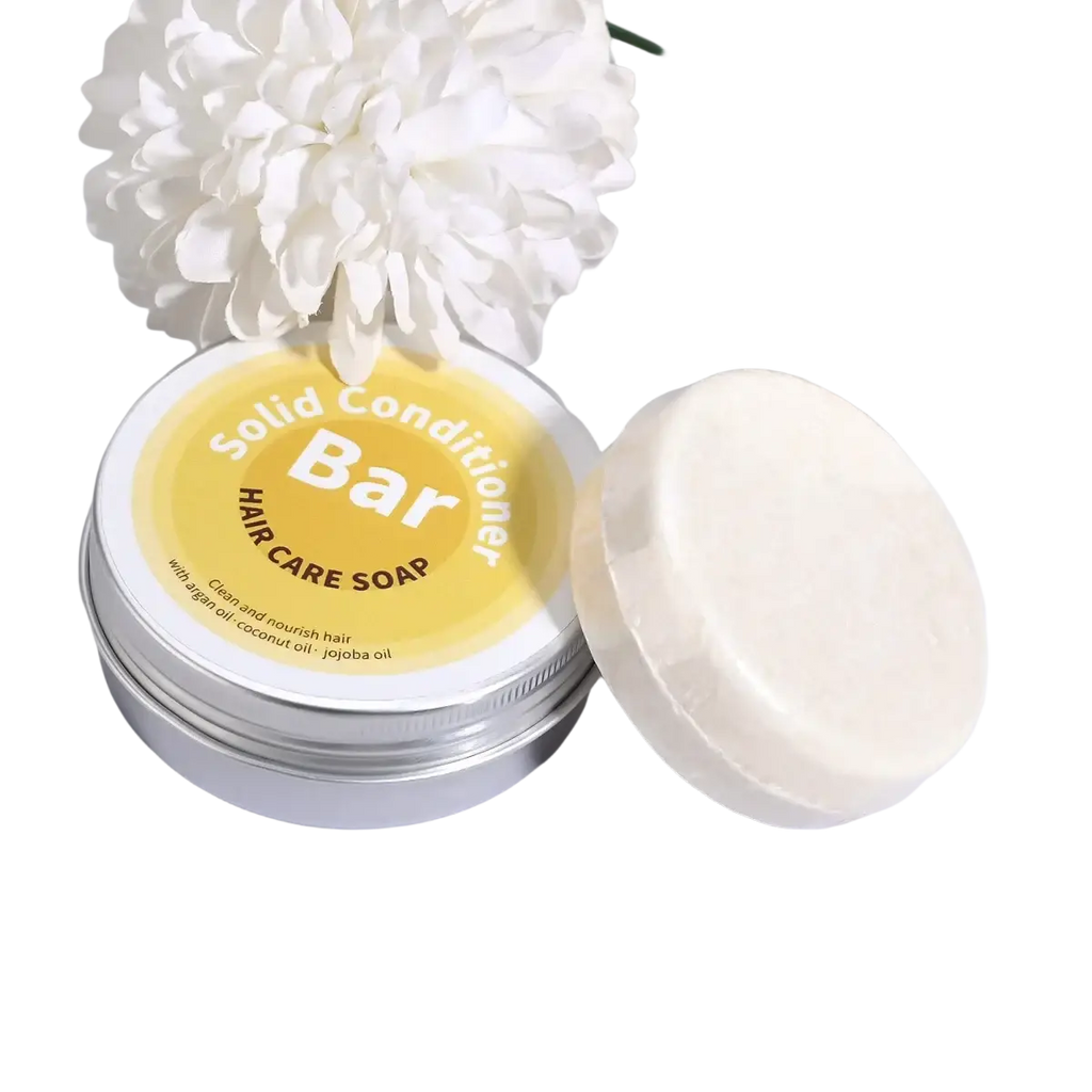 A creamy white argan oil coconut oil jojoba solid conditioner bar beside a silver tin with a yellow label