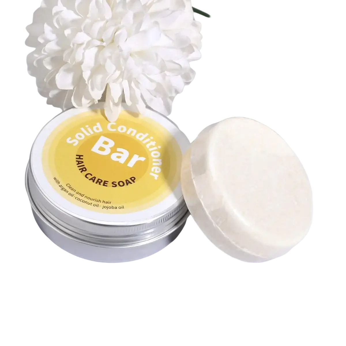 A creamy white argan oil coconut oil jojoba solid conditioner bar beside a silver tin with a yellow label