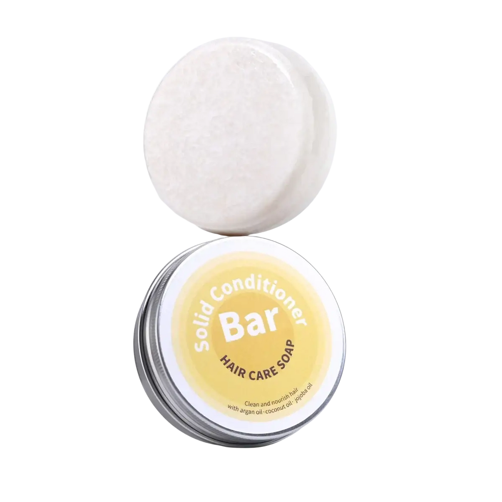 White circular solid conditioner bar with argan oil coconut oil jojoba resting on a silver tin with yellow label