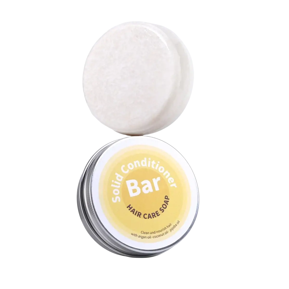 White circular solid conditioner bar with argan oil coconut oil jojoba resting on a silver tin with yellow label