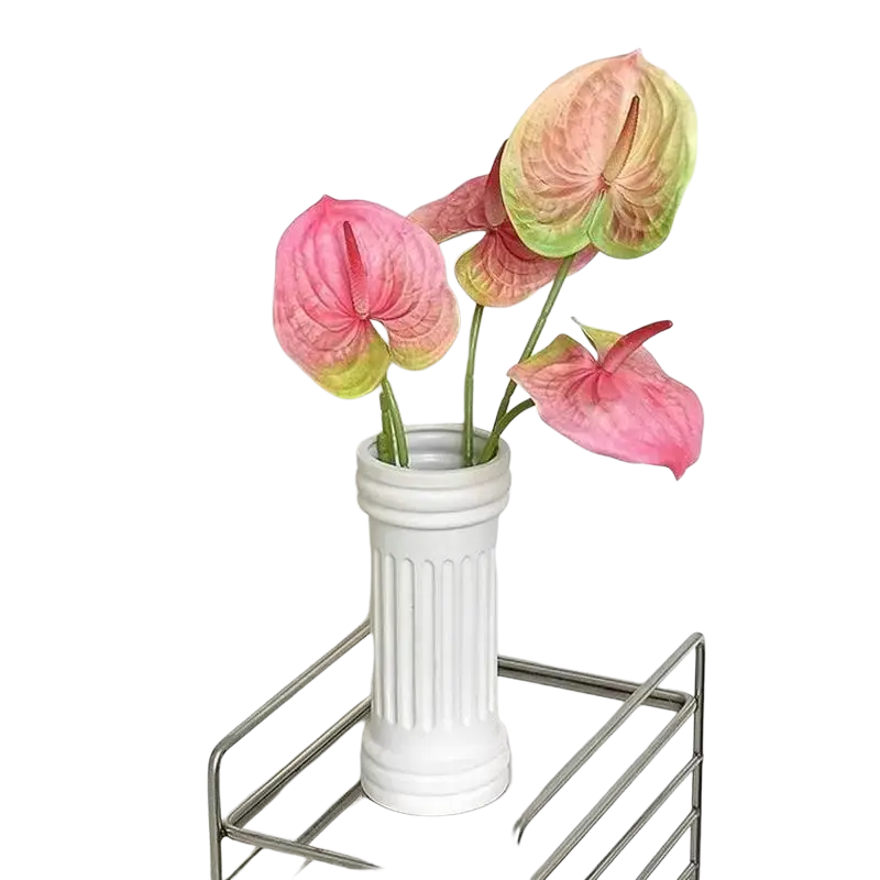 White ceramic vase with vertical fluting and classic columnar shape holding artificial anthurium flower bouquet