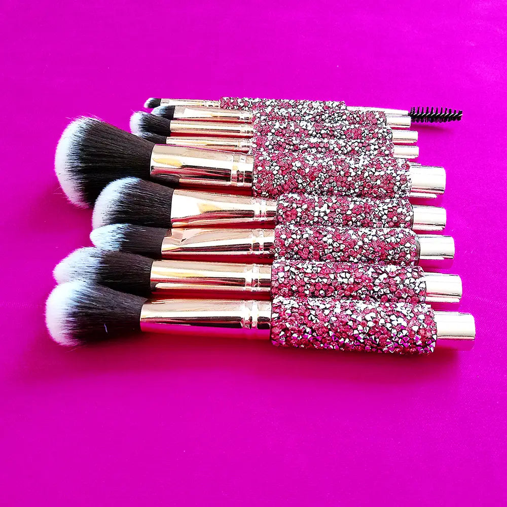 Set of 10 rhinestone makeup brushes with rose gold ferrules and handles encrusted in pink and silver rhinestones included in a pink makeup brush bag.
