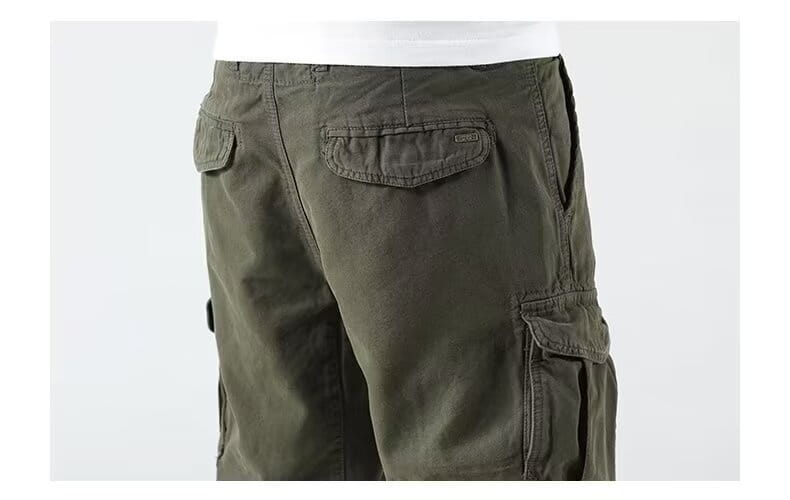 Men’s relaxed fit olive green cargo shorts made of durable material featuring multiple pockets and a subtle brand patch on the back right pocket, shown from the back side.