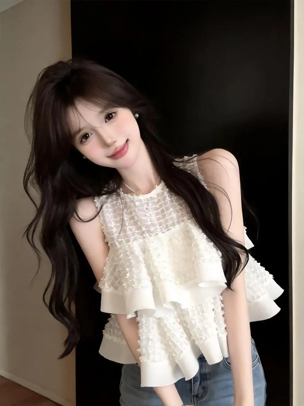 Blusa negra sin mangas con volante fruncido que presenta un diseño de volante en capas, una sección superior tejida con textura y detalles delicados de encaje en blanco.