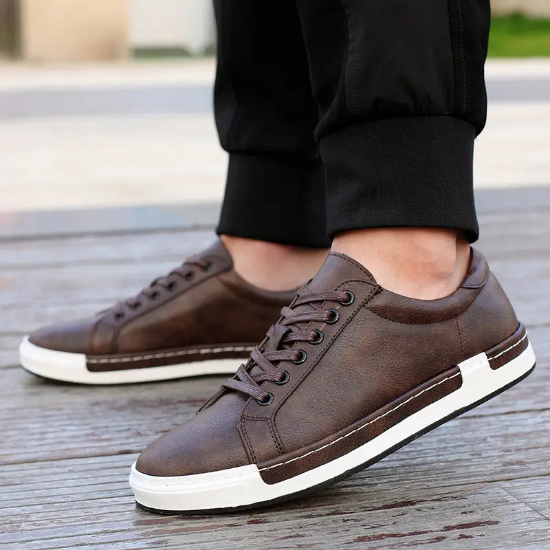 Les baskets basses en cuir pour homme, faites à la main, présentent des dessus en cuir marron, des semelles en caoutchouc blanc et des coutures contrastantes, pour un usage décontracté.