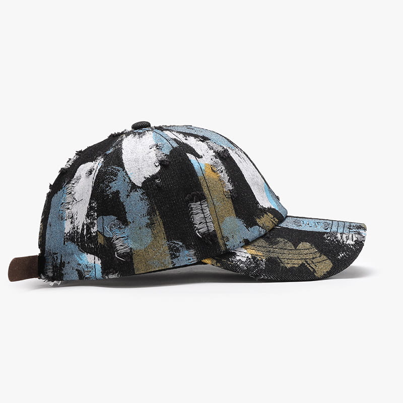 Une casquette de baseball en coton à projections de peinture vieillies, présentant un design abstrait audacieux dans des tons noir, blanc, bleu et beige.