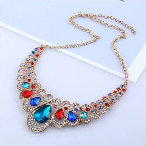Vintage gold teardrop crystal bridal jewelry set featuring a vibrant gold-toned statement necklace with a cascading design of large blue and red teardrop crystals surrounded by clear rhinestones.