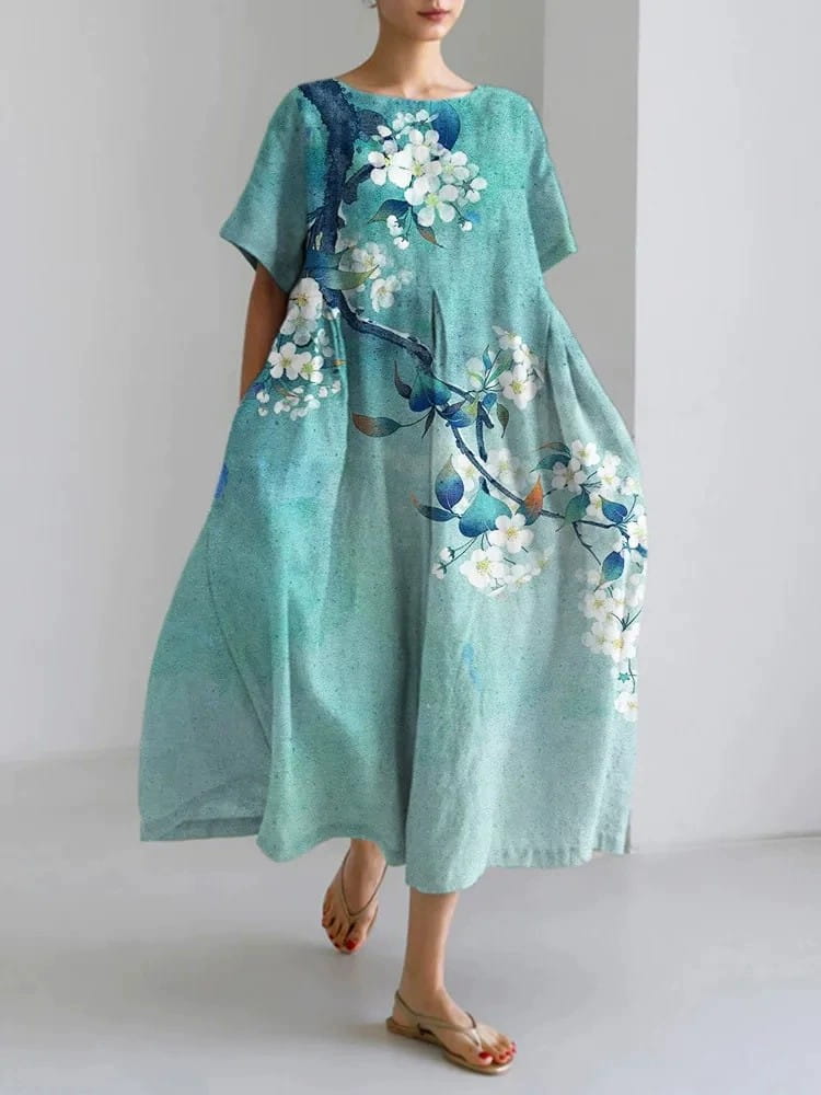 A flowing teal linen maxi dress with a delicate white floral pattern and dark blue branches featuring an artistic printed design.