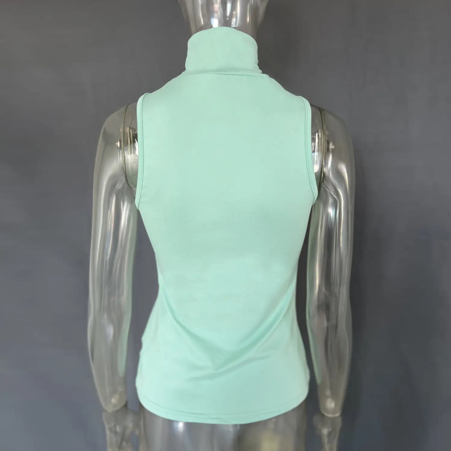 A mint green sleeveless stretch turtleneck top with a gold ring halter detail displayed on a mannequin.