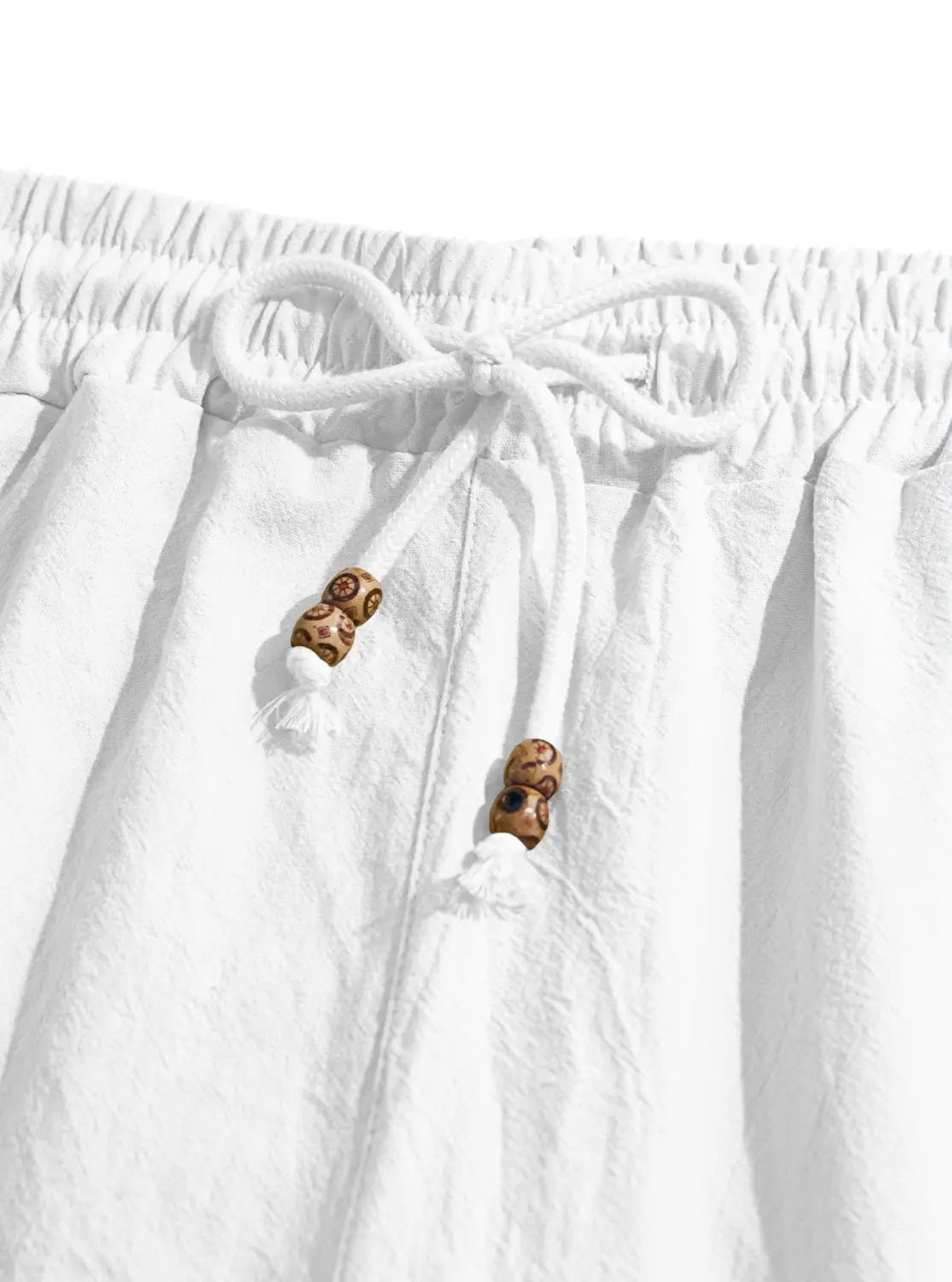 White cotton linen mens drawstring shorts featuring wooden beads and tassels on the cord.