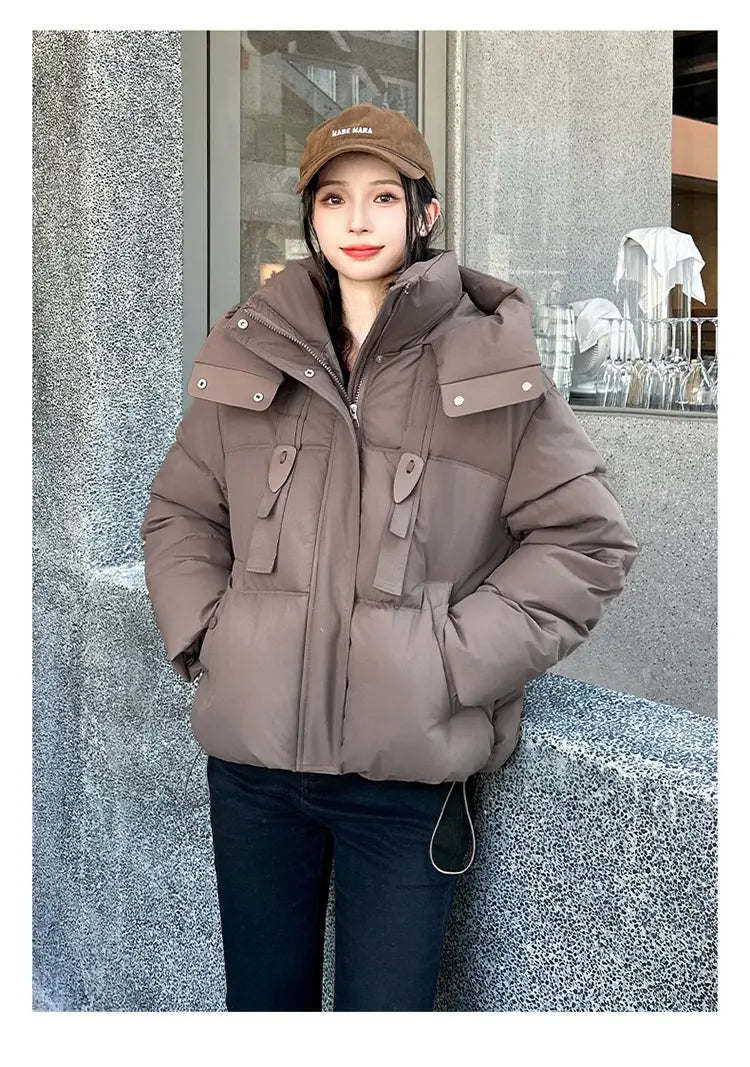 Veste courte matelassée à capuche marron pour femme, confortable et volumineuse, avec poches avant, conçue comme un manteau d’hiver chaud.