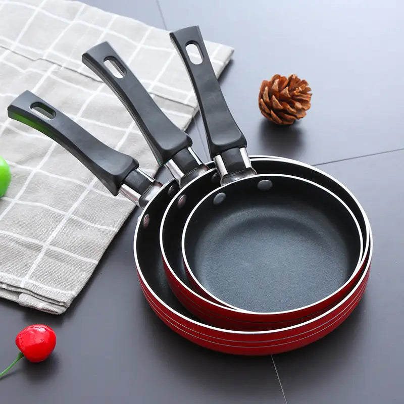 Set of three nested red aluminum mini non-stick frying pans with black handles for cookware.
