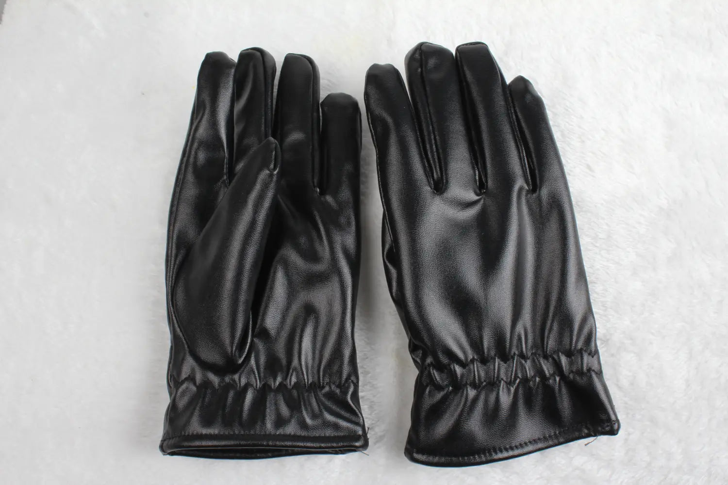 Une paire de gants d’hiver en cuir noir élégants à la finition lisse et brillante et aux poignets élastiqués, conçus pour être chauds et coupe-vent pour un usage unisexe.