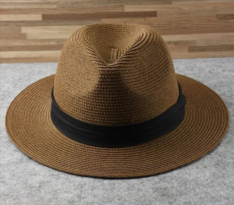 A tan woven straw fedora hat with a wide brim and a black satin band designed for foldable sun protection for men.