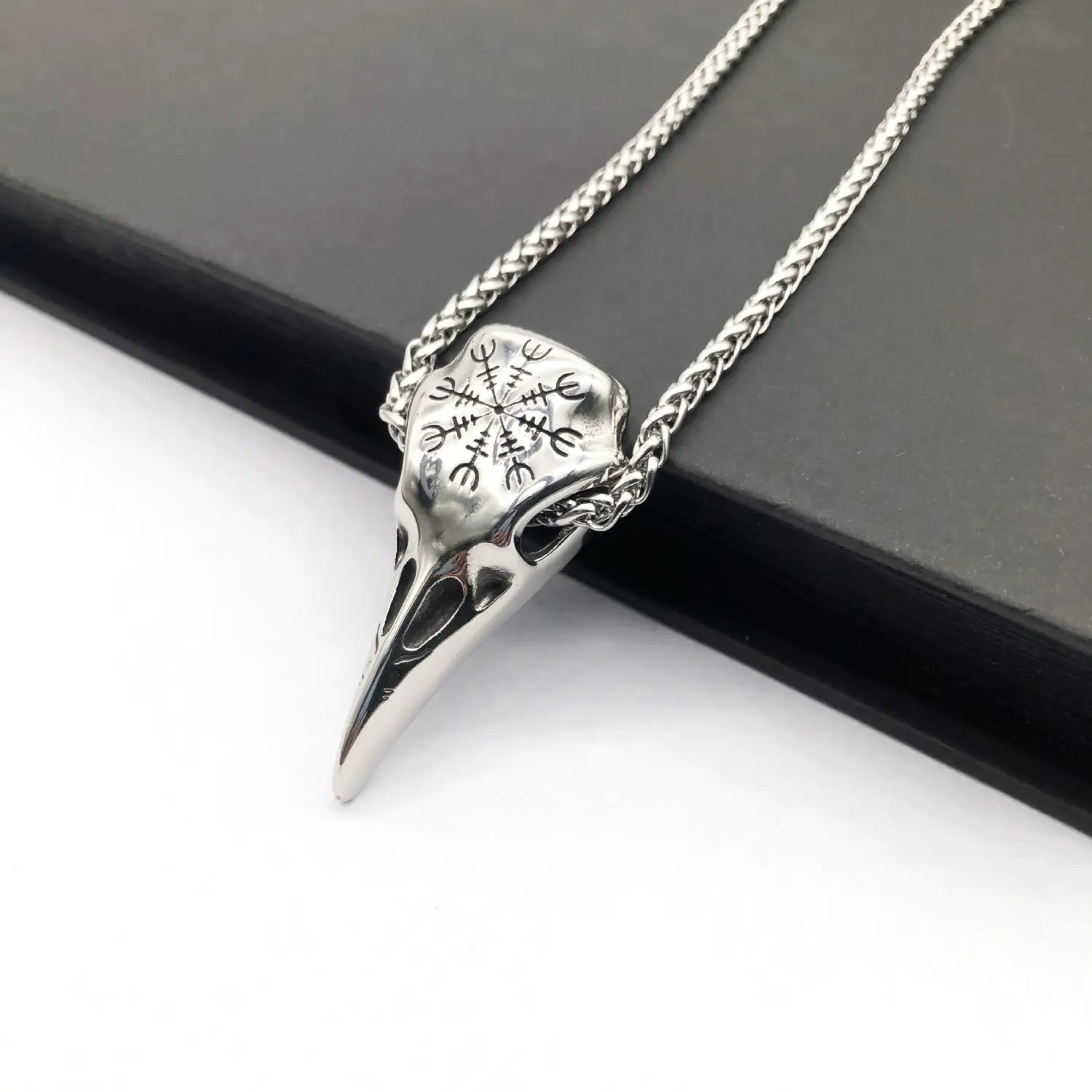 Silver vintage Viking runic raven skull pendant necklace with intricate runic engraving on the forehead suspended from a matching braided chain.