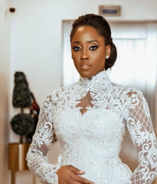 A woman wearing an elegant white floral lace stand collar wedding gown with long sleeves and a high neckline.
