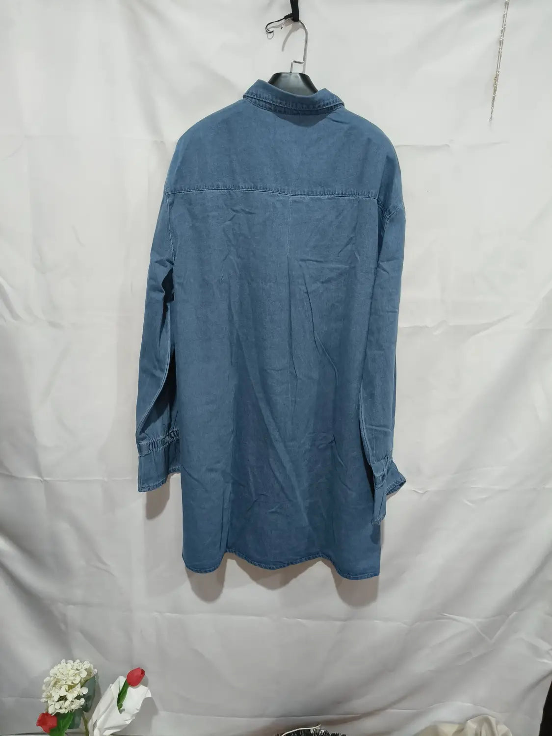 Blaues Jeanshemd mit klassischem Kragen und langen Ärmeln, das an einem Bügel zu sehen ist, dargestellt als Produkt in einem lockeren Langarm-Jeanshemdkleid im A-Linien-Schnitt.