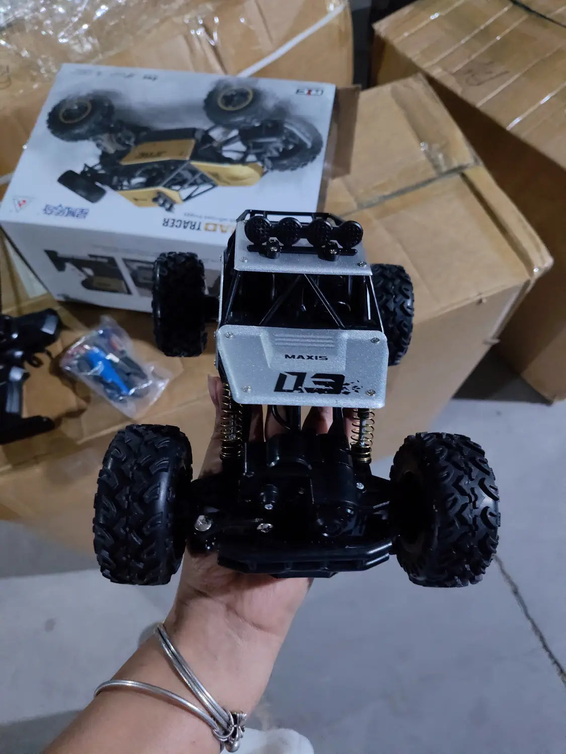 Camion teledirigido RC todoterreno 4WD de alta velocidad en negro y blanco, tipo crawler, con neumáticos resistentes, chasis detallado y la marca Maxis 03 en la parte frontal.